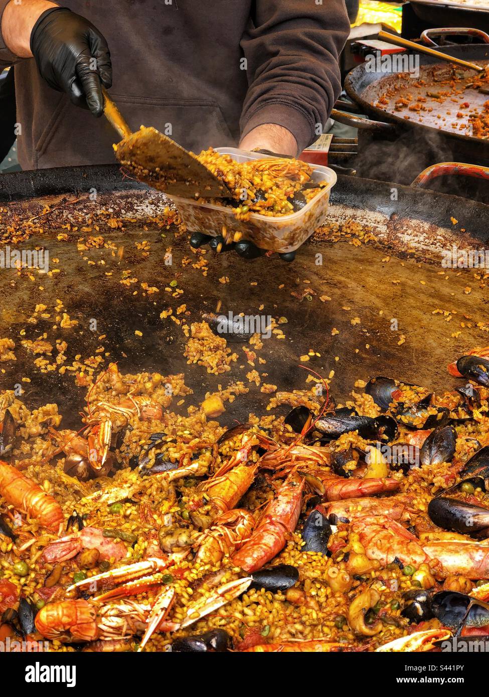 Serve una porzione da una paella in paella cucinare frutti di mare spagnolo paella Street food all'aperto presso il mercato agricolo locale nel Regno Unito - Immagine stock catturata con smartphone