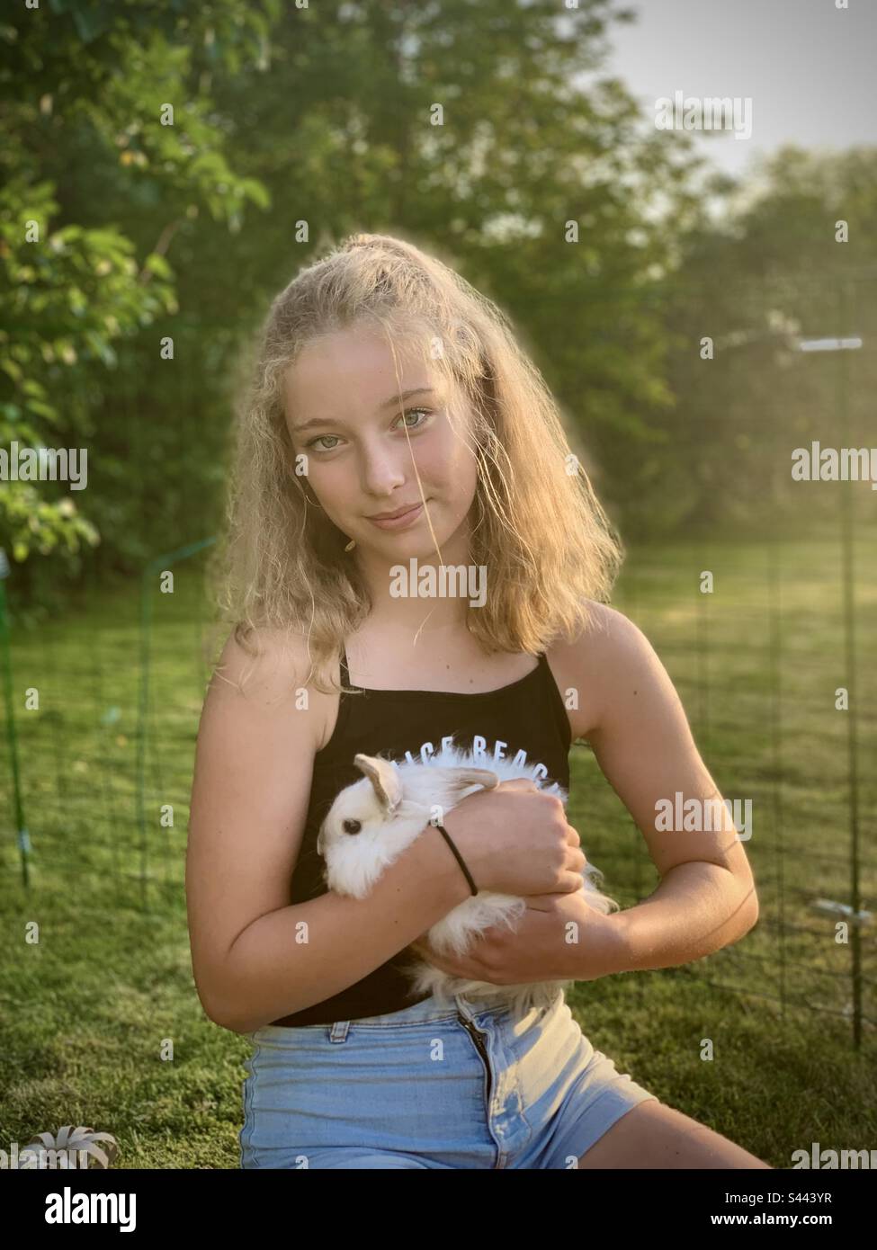 Una giovane ragazza carina di 10 anni posa nel suo giardino abbracciando il suo animale domestico coniglietto bianco coniglio felice amante sorridente animale Foto Stock