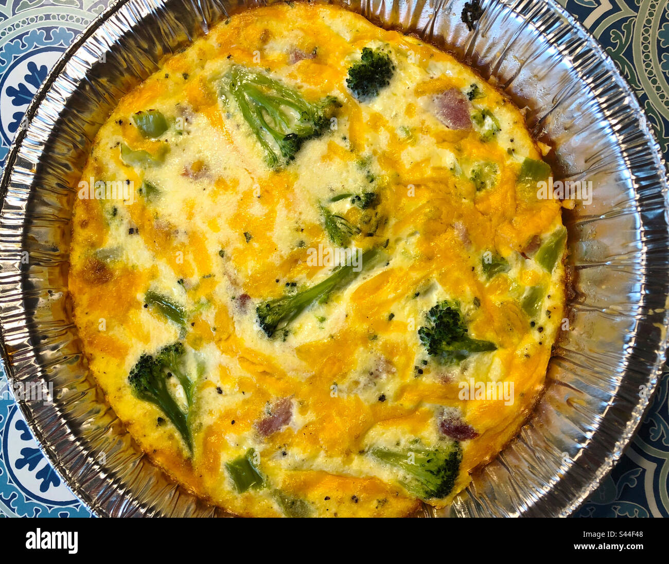 Una sana quiche croccante fatta con uova, formaggio di contadino, prosciutto e broccoli e ricoperta con formaggio cheddar prima di essere cotta. - Immagine stock catturata con smartphone