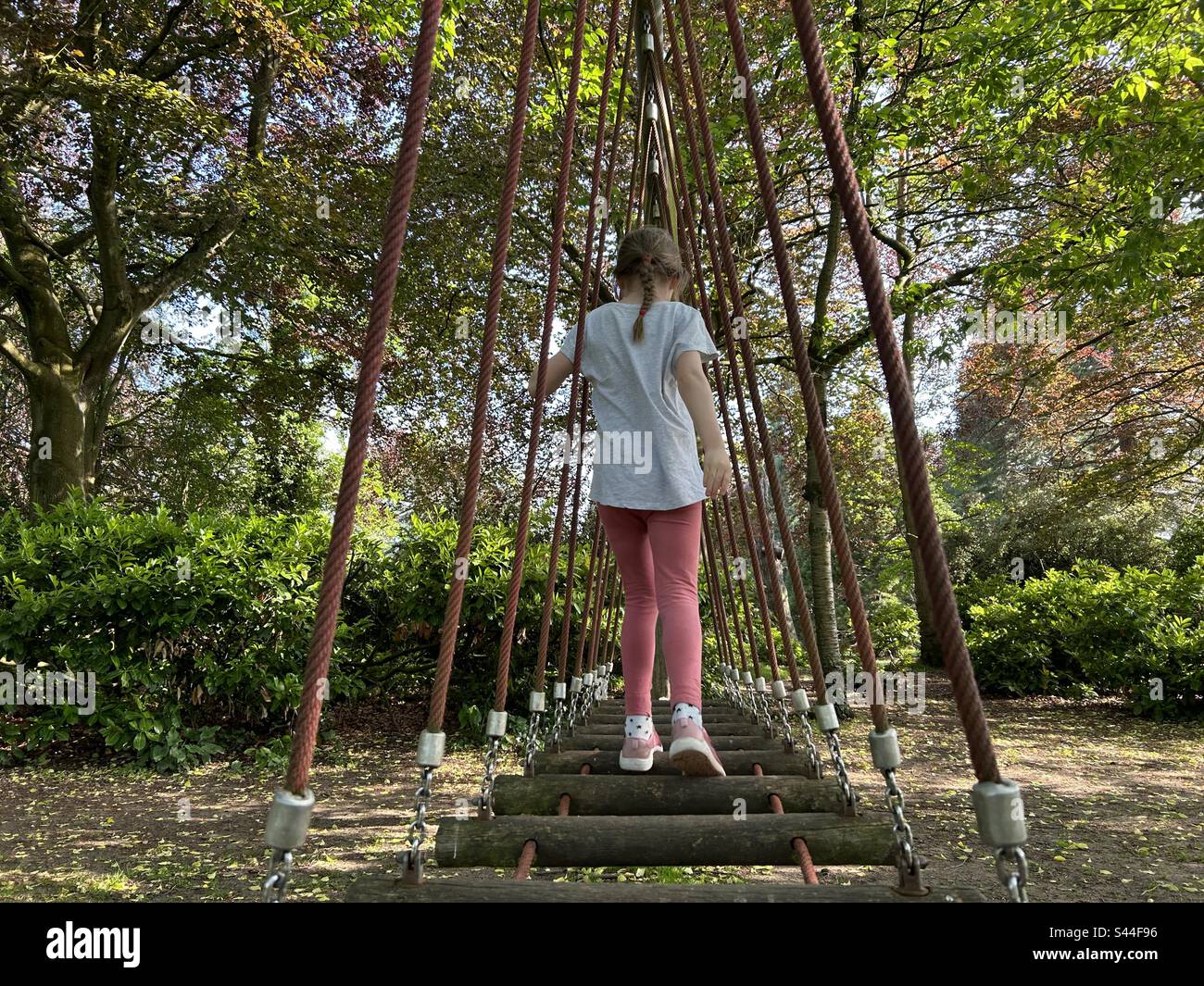 Ragazza in un'area giochi nel bosco, camminando lungo una scala di tronchi swing ponte Foto Stock