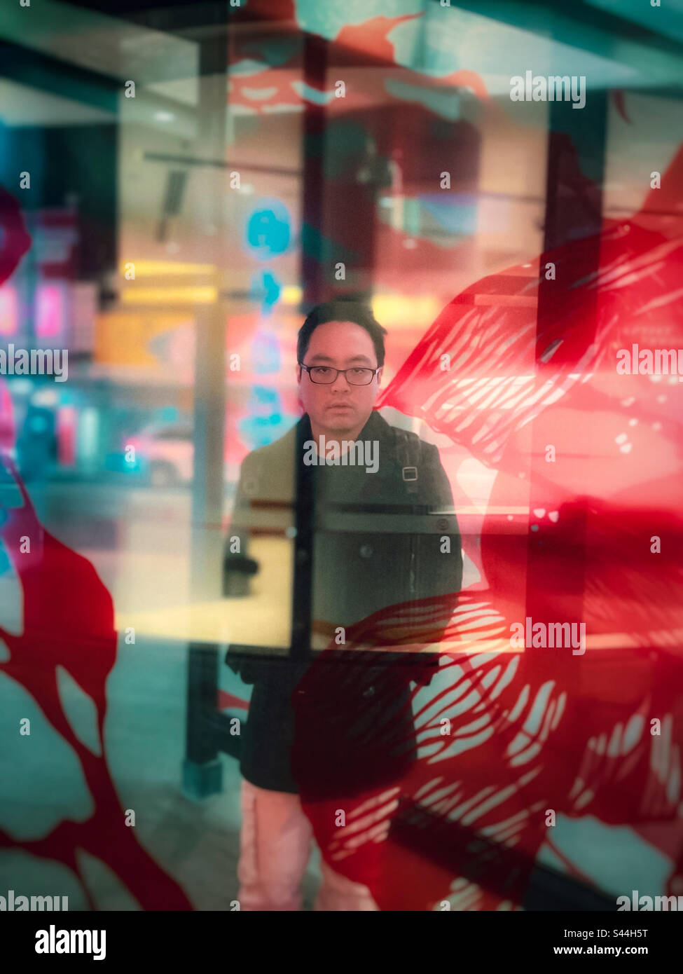 Diversi livelli di realtà. Ritratto di un giovane asiatico dietro uno schermo di vetro con riflessi e illuminazione al neon sulla strada cittadina di notte. Surreale. Sognante. - Immagine stock catturata con smartphone