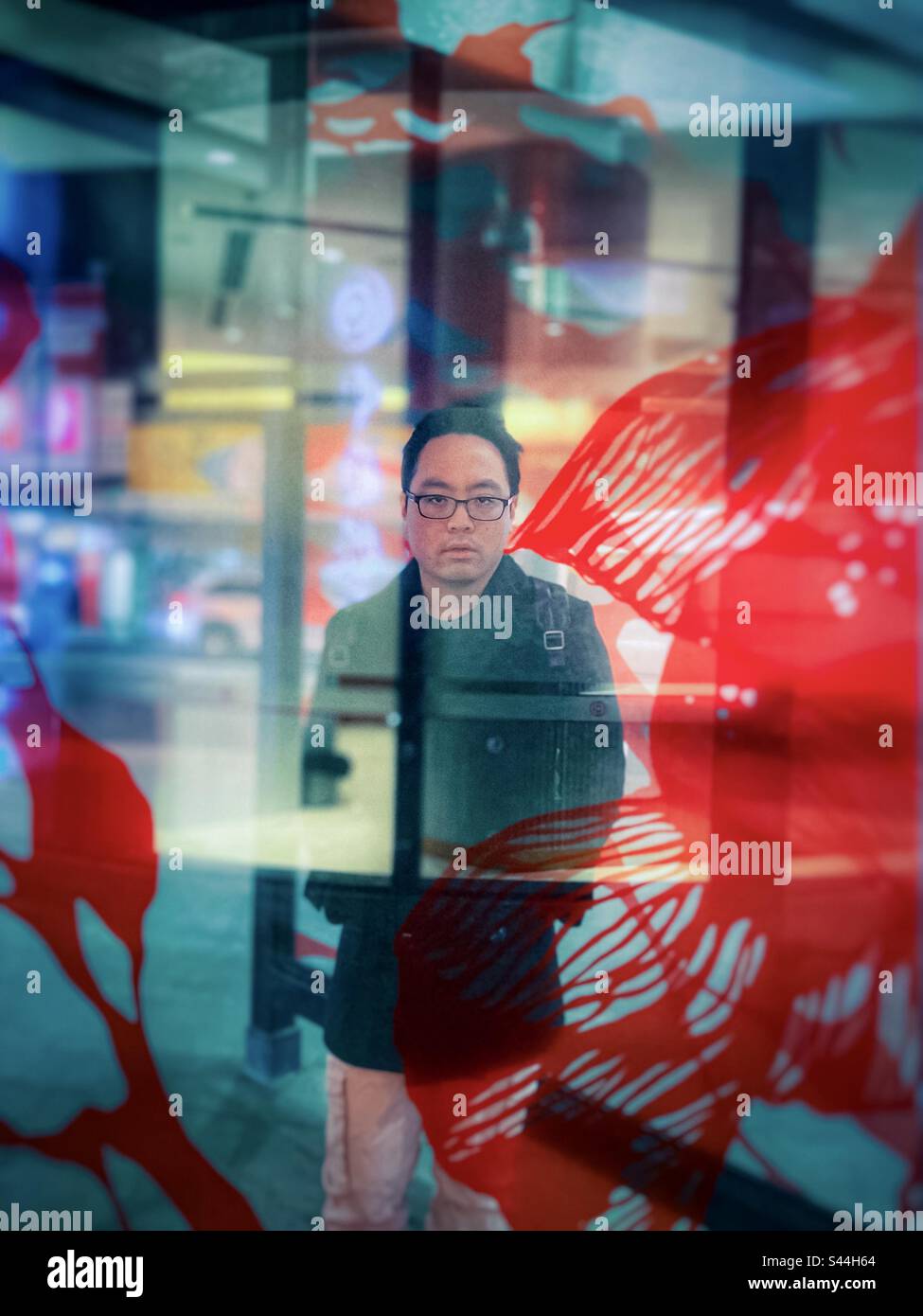 Diversi livelli di realtà. Ritratto di un giovane asiatico dietro uno schermo di vetro con riflessi e illuminazione al neon sulla strada cittadina di notte. Surreale. Sognante. - Immagine stock catturata con smartphone