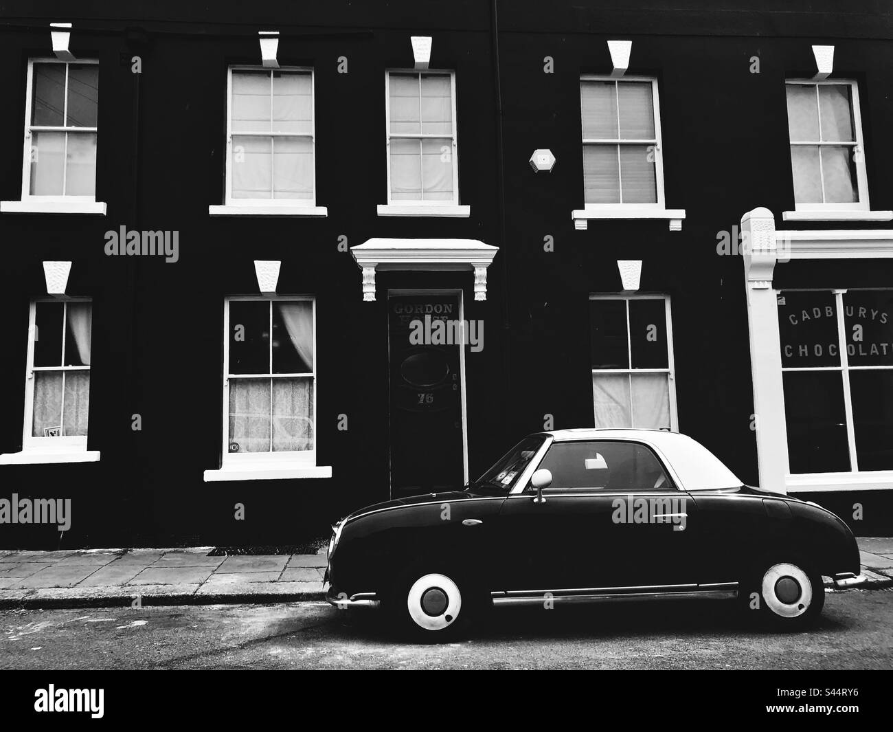 Auto in stile vintage in bianco e nero parcheggiata da un edificio dipinto in bianco e nero Foto Stock