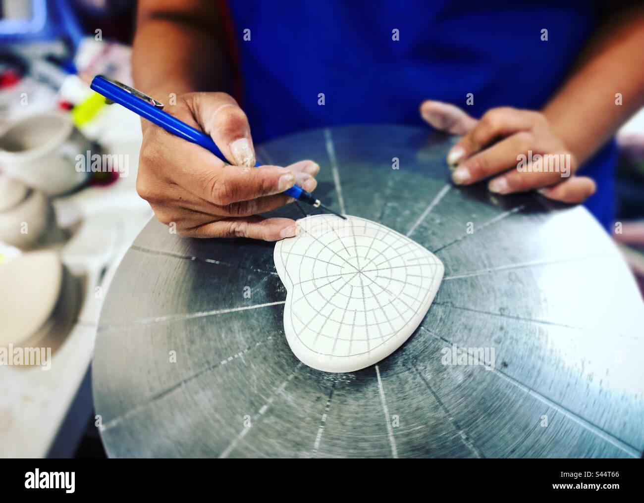 Una donna che dipinge un'opera di ceramica in un laboratorio artigianale di ceramica Servin a Villa Progreso, Ezequiel Montes, Queretaro, Messico - Immagine stock catturata con smartphone