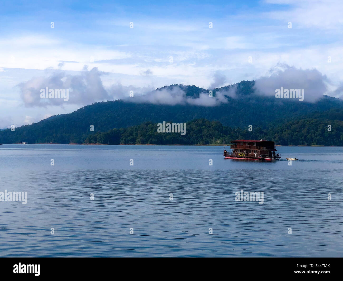 Casa galleggiante sul lago artificiale di Kenyir Terengganu, nuvole visibili che galleggiano sulla cima della casa galleggiante, acqua calma, alberi e colline sullo sfondo. Foto Stock