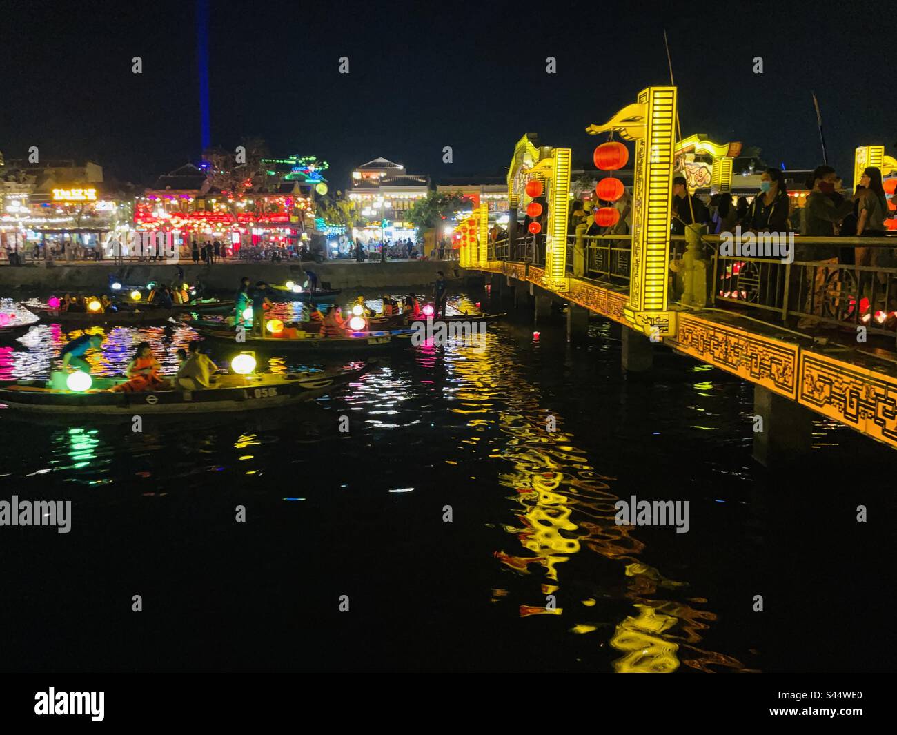 Vista serale di un mercato notturno in Vietnam che circonda le barche che galleggiano lungo un fiume. Foto Stock