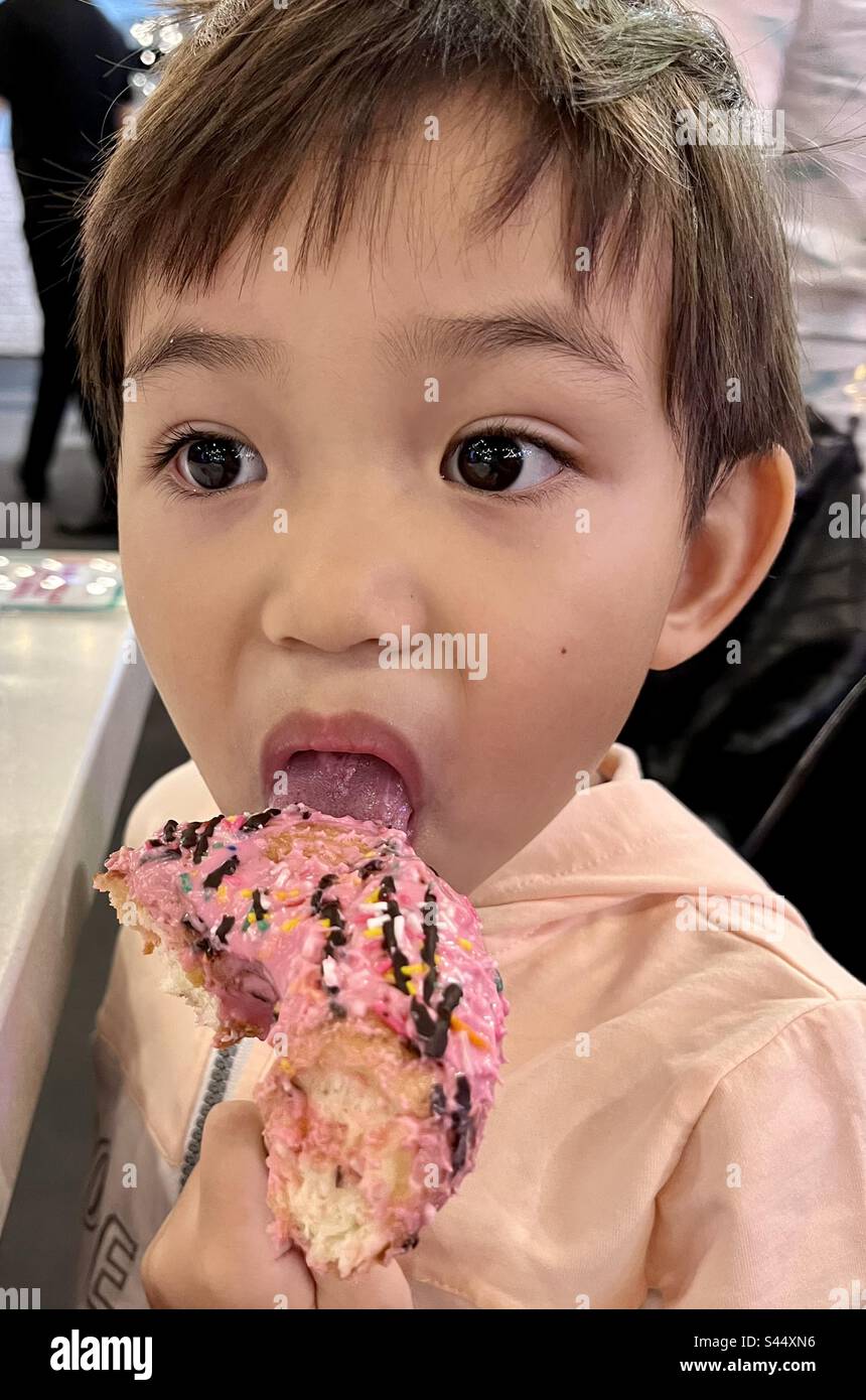 Bambino che mangia ciambella rosa con gli spruzzi Foto Stock