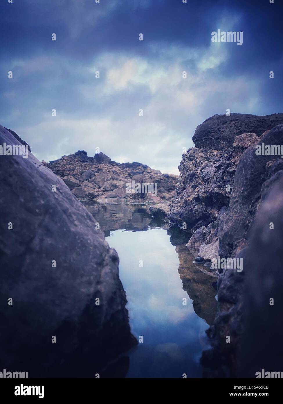 Una fotografia di una piscina di roccia da una prospettiva bassa. Riflessi sulla superficie dell'acqua. Tema litoraneo dell'oceano. Foto Stock