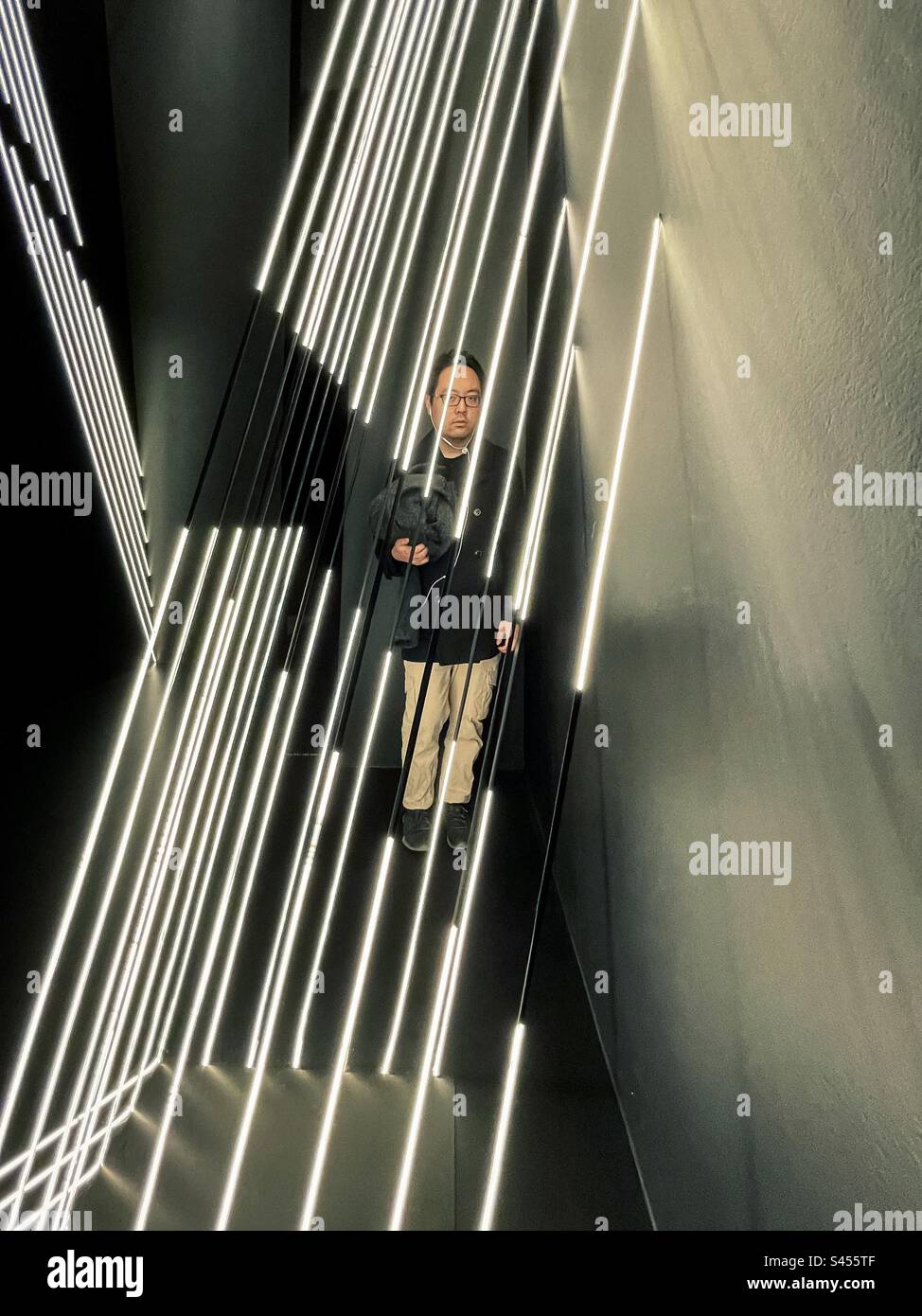 Giovane uomo in piedi all'interno di un'installazione di nastro luminoso, Sky Whispers di Meagan Streader a Melbourne Now Exhibition presso Ian Potter Centre: NGV Australia, Melbourne, marzo-agosto 2023. Luce e architettura - Immagine stock catturata con smartphone