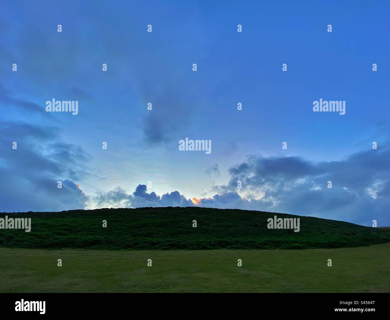 Una fotografia di un paesaggio - un campo verde e una collina con un'alba nascosta dietro. Cielo blu, spazio copia Foto Stock