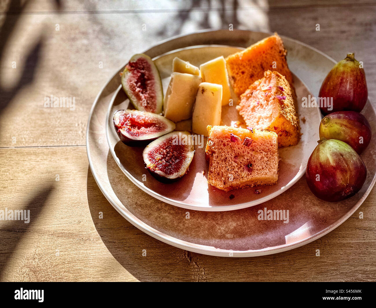 Primo piano di fichi freschi, interi e affettati, formaggio e fette di torta al chiffon di rosa su piatti a tavola. Snack, dessert. - Immagine stock catturata con smartphone