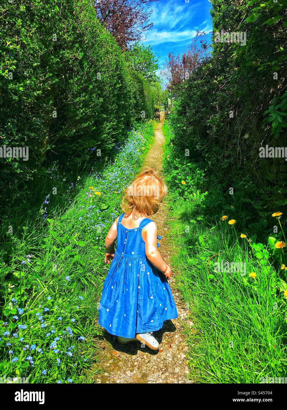 Bambina che esplora il suo villaggio fiancheggiata da colore e fiori selvatici Foto Stock