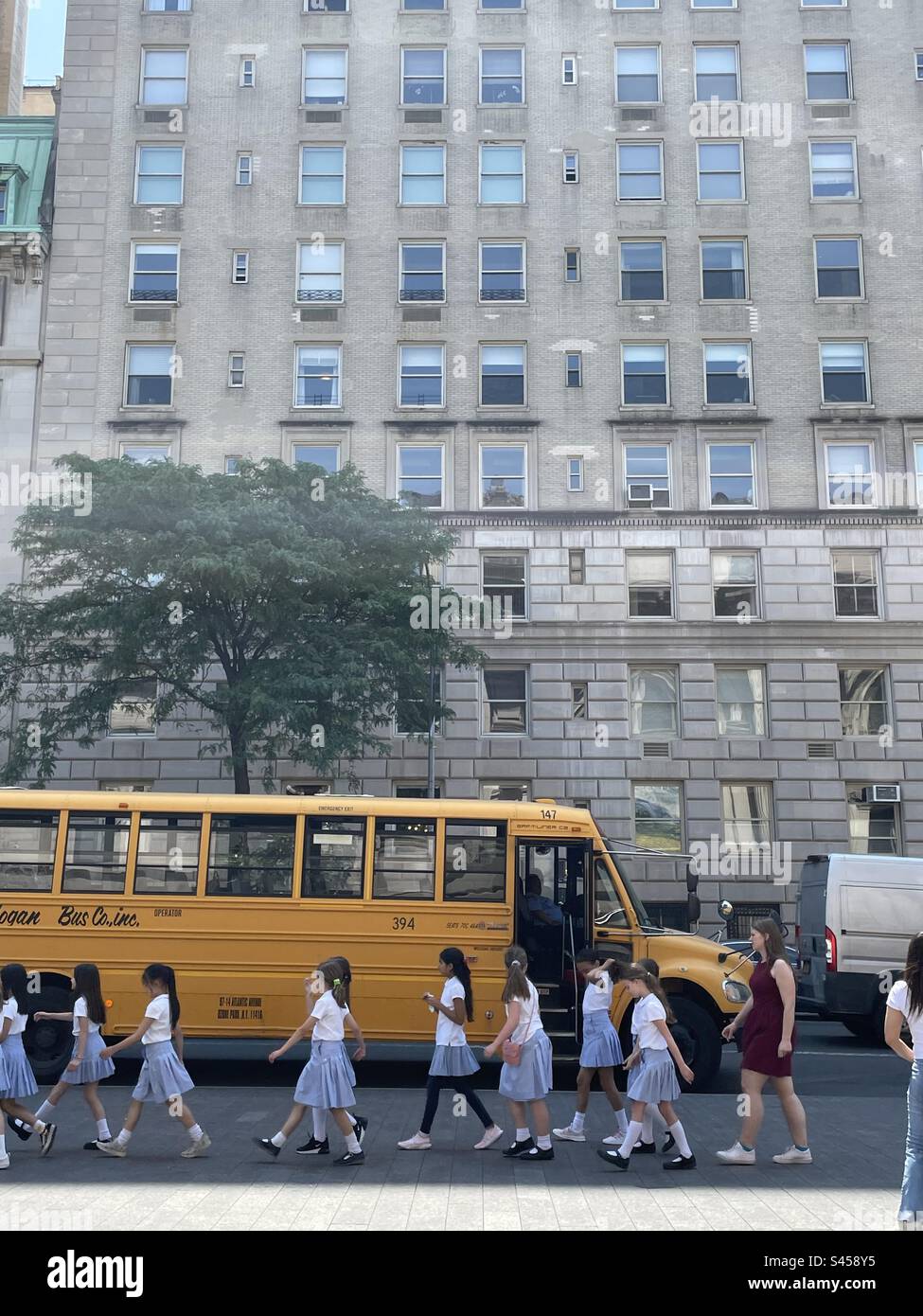 I bambini delle scuole camminano davanti al loro autobus parcheggiato di fronte a un condominio a New York Foto Stock