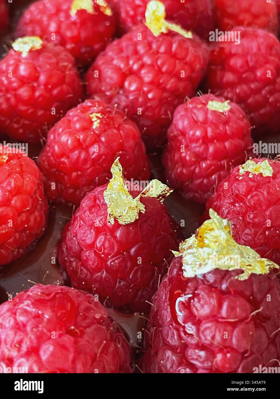 Lamponi freschi con fiocchi d'oro su una torta al cioccolato - Immagine stock catturata con smartphone