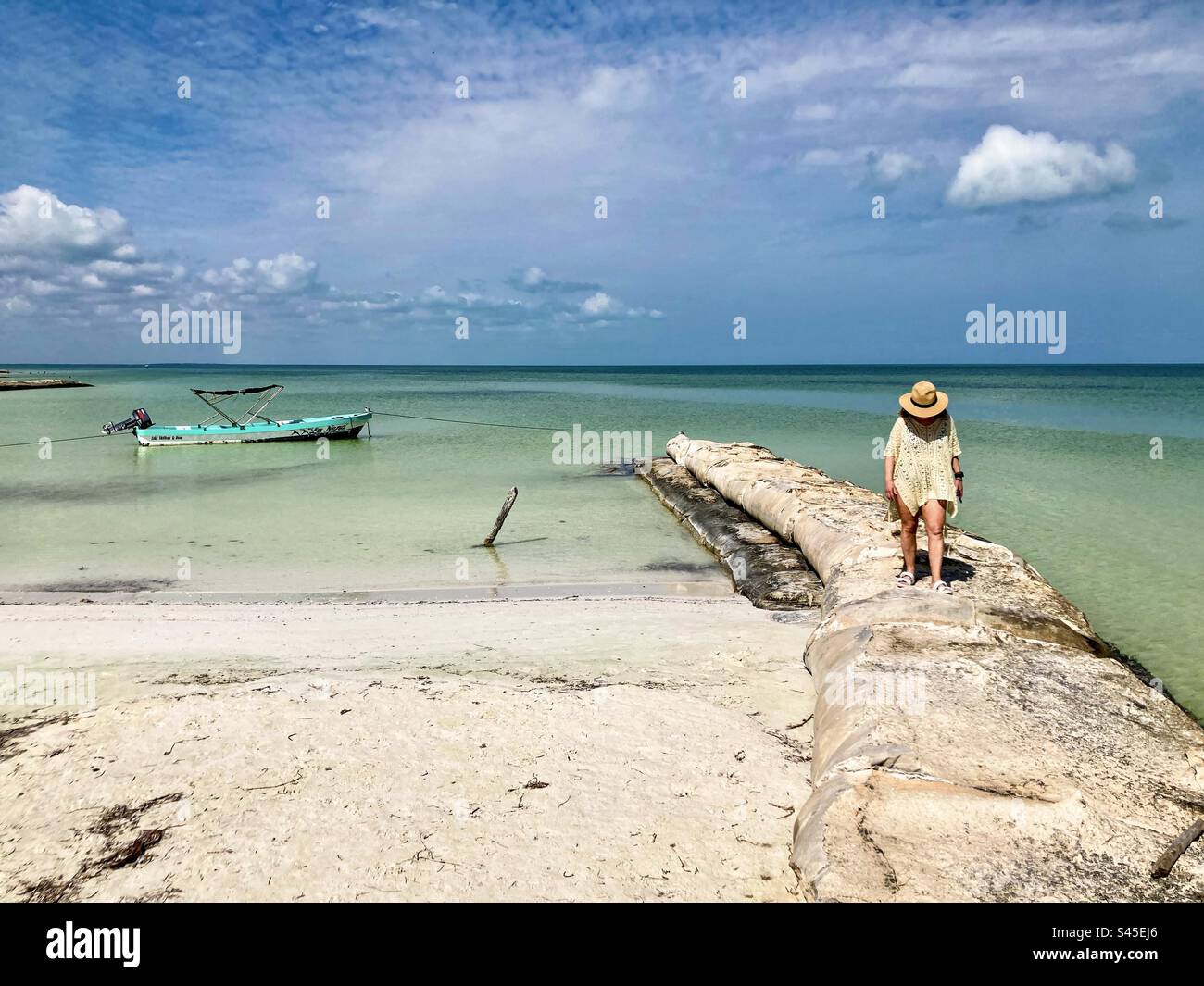 Una donna cammina lungo un rompionde sulla spiaggia di Holbox. Foto Stock