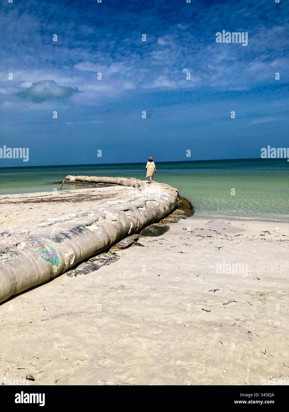 Una donna cammina lungo un rompigranella sulla spiaggia di Holbox. Foto Stock