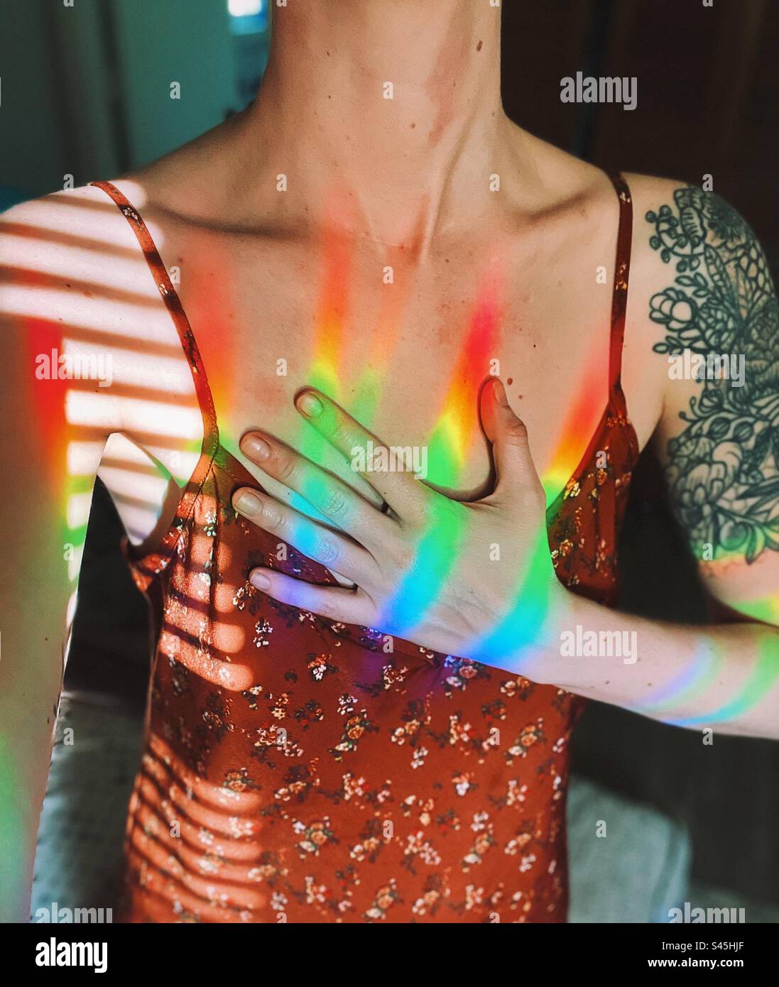 Donna che tiene la mano sul cuore con la luce dell'arcobaleno Foto Stock