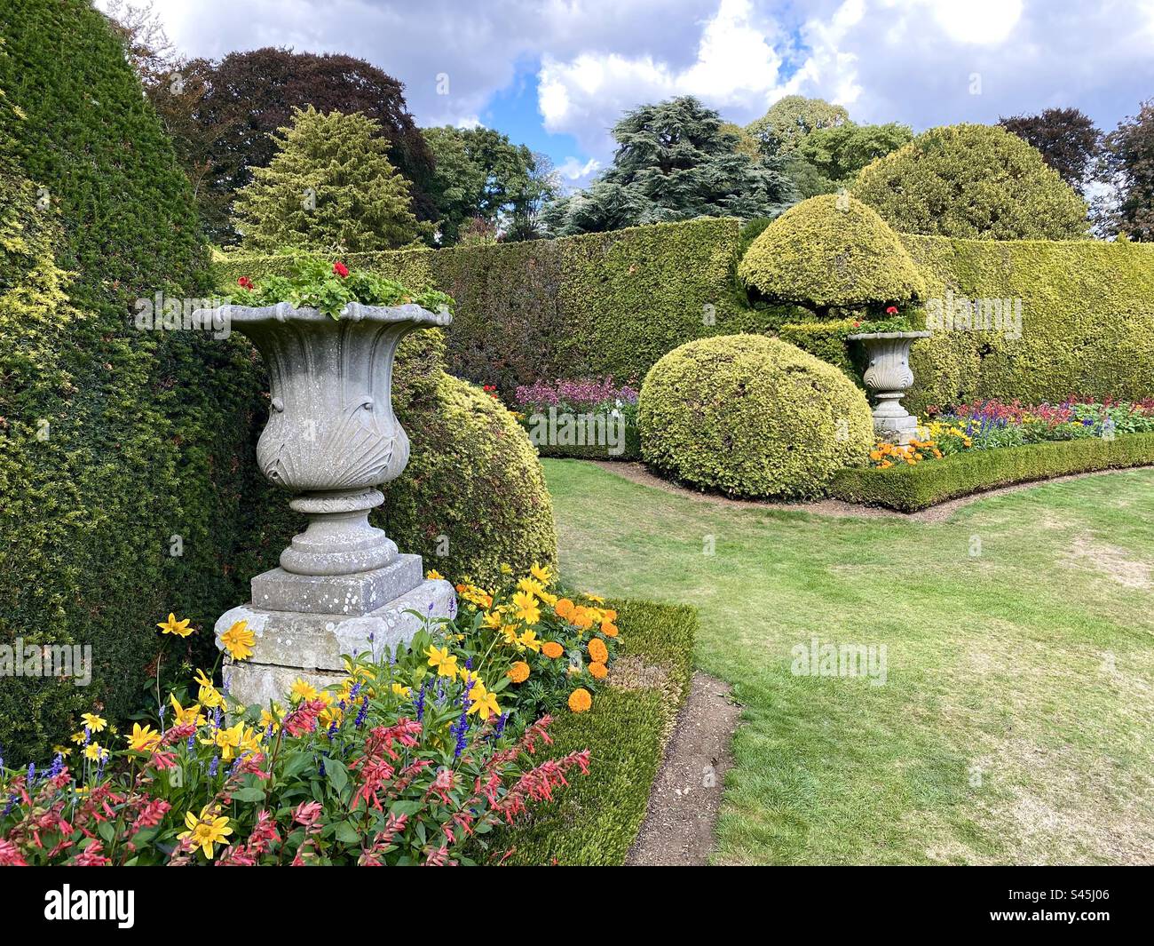 Bellissimi fiori estivi e piantatrici decorative in pietra in un giardino formale in Inghilterra Foto Stock