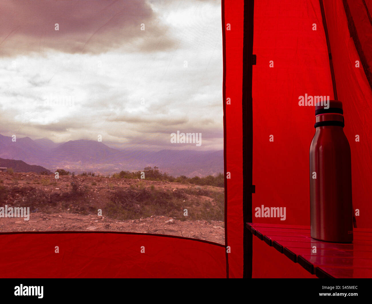Bottiglia termica su un tavolo da campeggio all'interno di una tenda rossa in un paesaggio montano. - Immagine stock catturata con smartphone