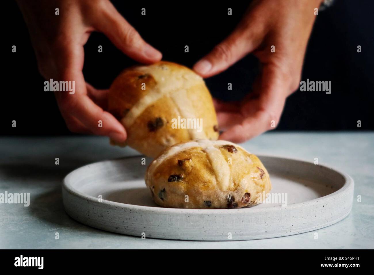 Le mani di una donna posizionano panini a croce caldi su un piatto - Immagine stock catturata con smartphone