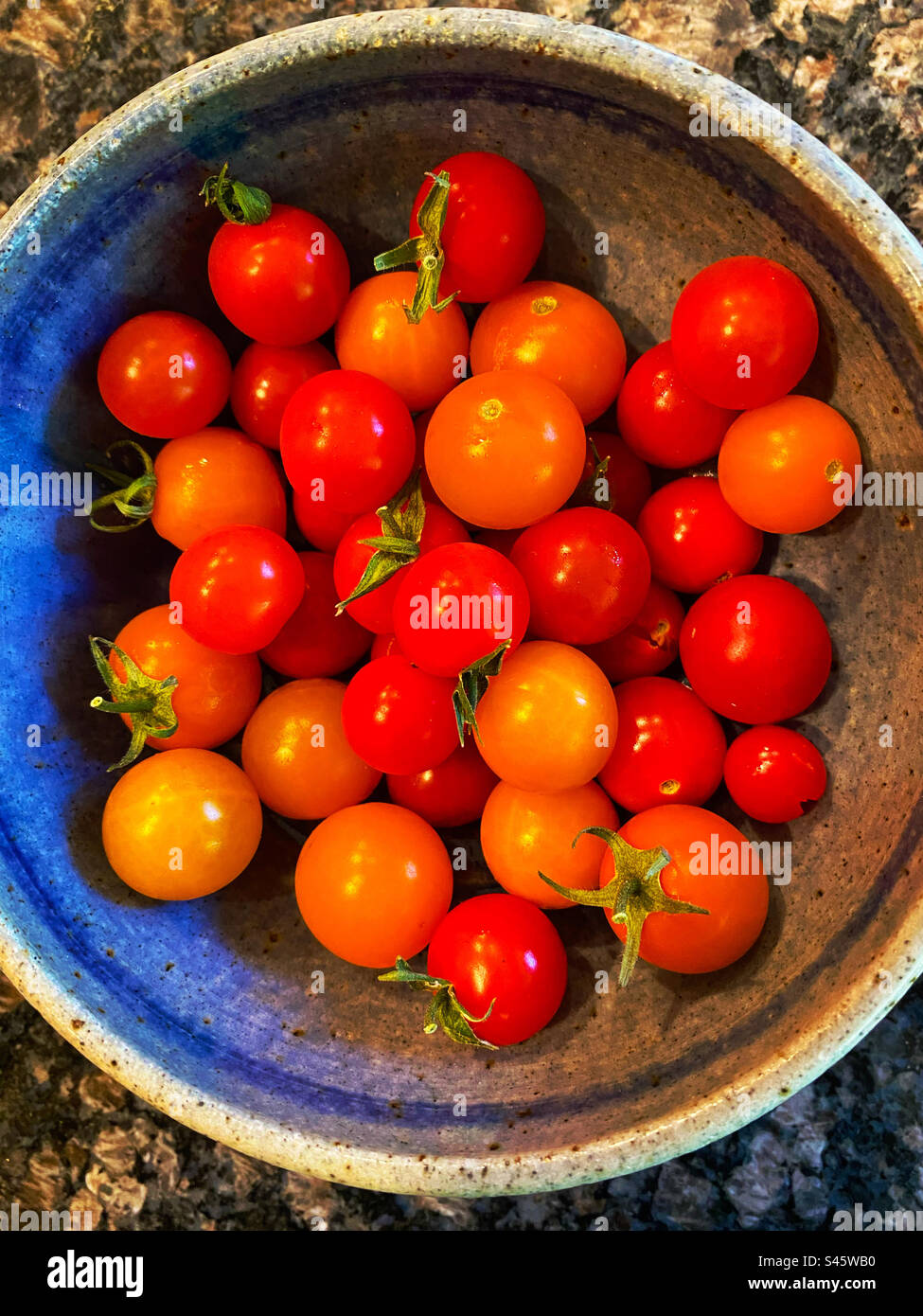 Pomodori ciliegini rossi e arancioni in un recipiente blu Foto Stock