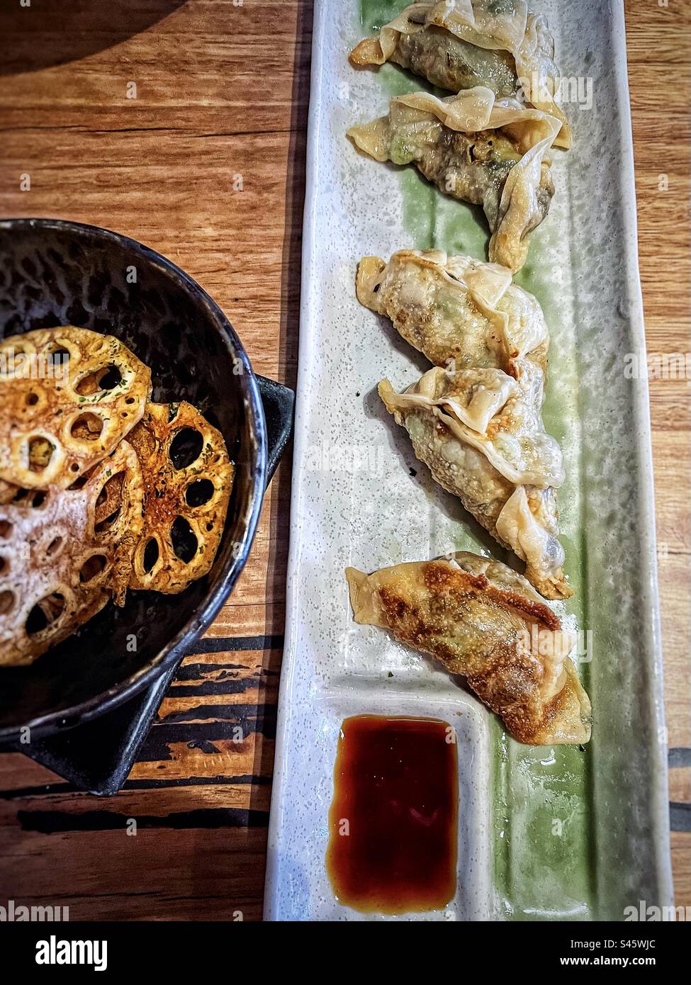Vista dall'alto della gyoza giapponese o degli gnocchi con salsa di soia immersi su un piatto accanto alle patatine di radice di loto in una ciotola sul tavolo. Foto Stock