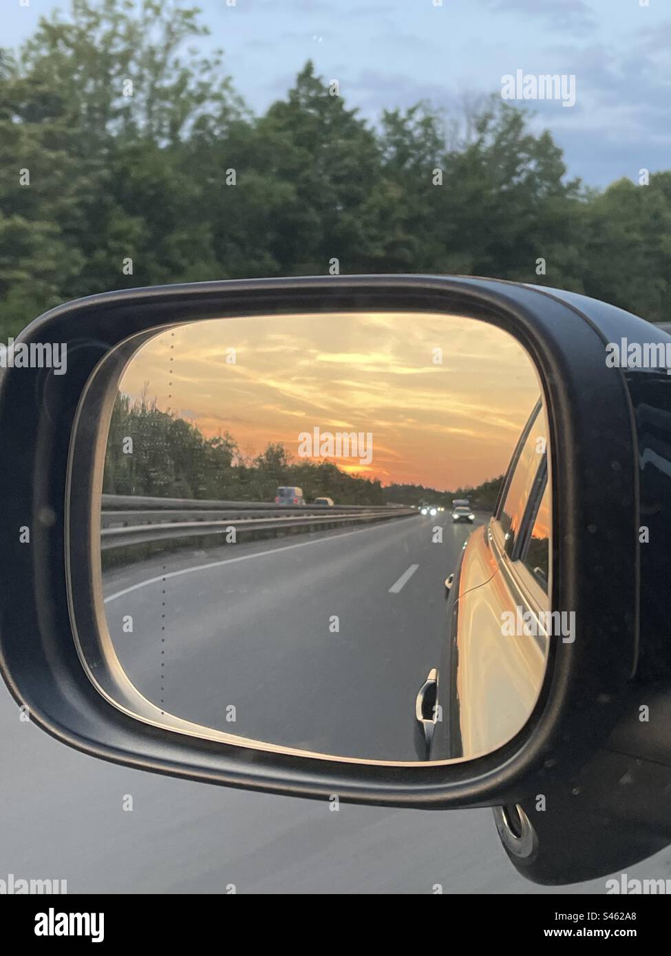 Il tramonto è raffigurato nello specchio dell'auto sull'autostrada - Immagine stock catturata con smartphone