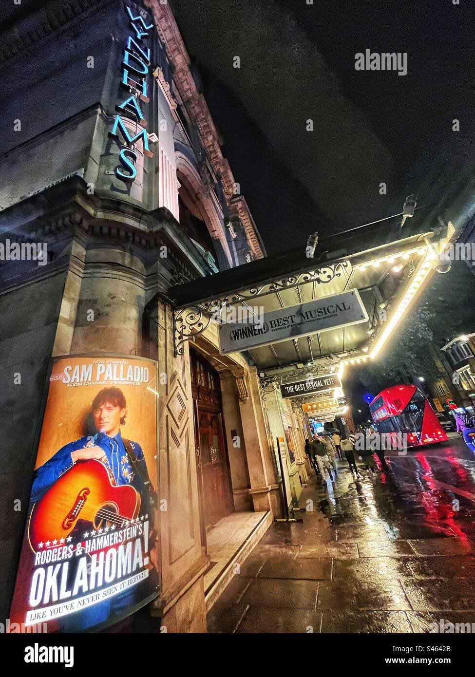 Il Wyndhams Theatre di Londra pubblicizza Oaklahoma visto di notte con la pioggia che si riflette sul marciapiede e l'autobus rosso sullo sfondo Foto Stock