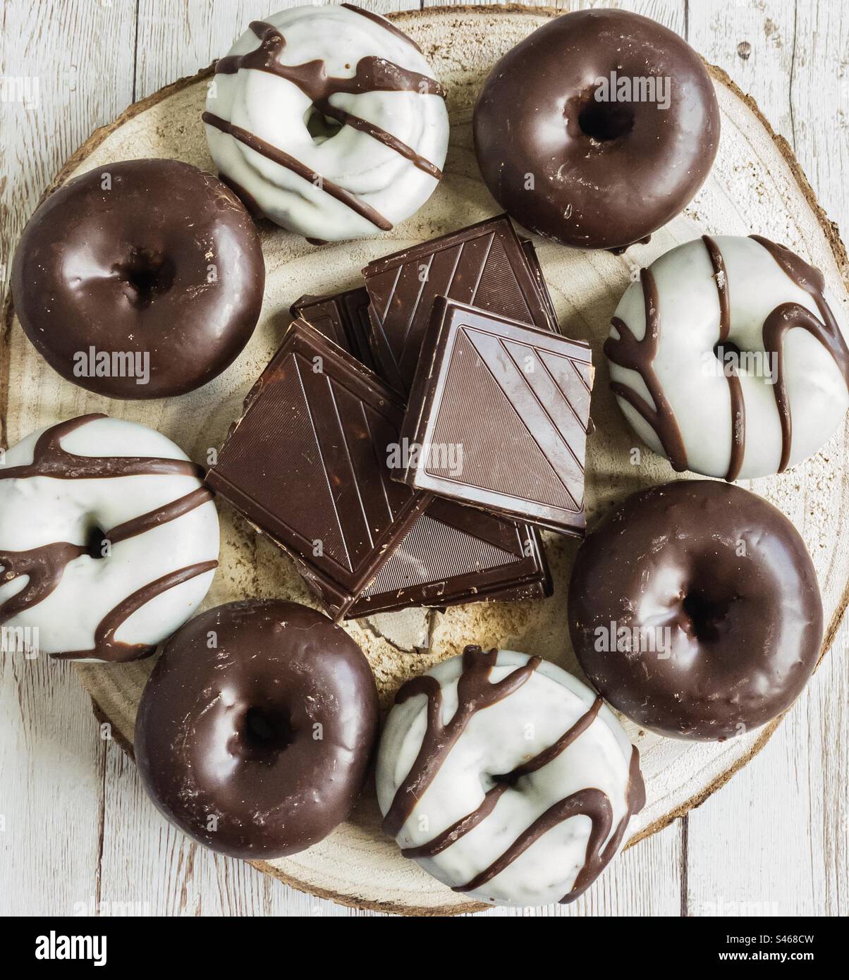 Ciambelle di cioccolato fondente e bianco, con pezzi di cioccolato su un piatto di legno Foto Stock