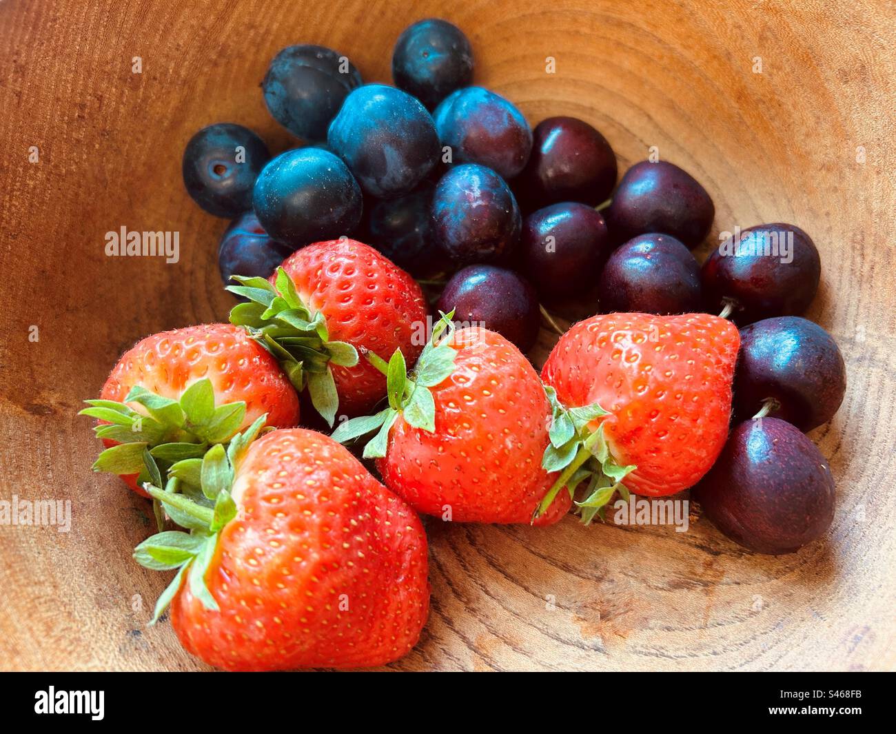 Cinque fragole, alcuni mirtilli e ciliegie in un recipiente di legno granato. Fresco, colorato, succoso, dolce, nutriente, frutta estiva. Foto Stock