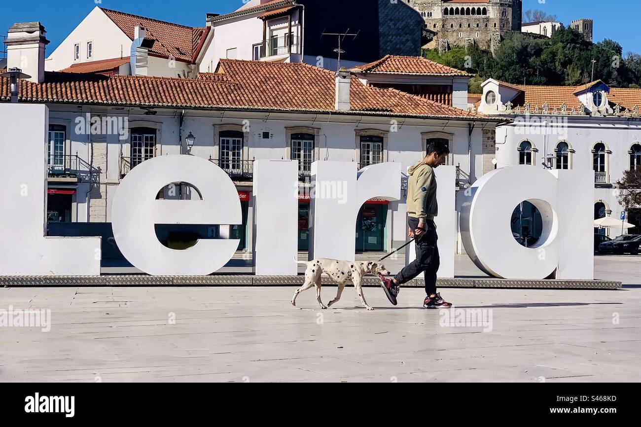 Un uomo cammina un dalmata davanti al grande cartello della città di Leiria - Immagine stock catturata con smartphone
