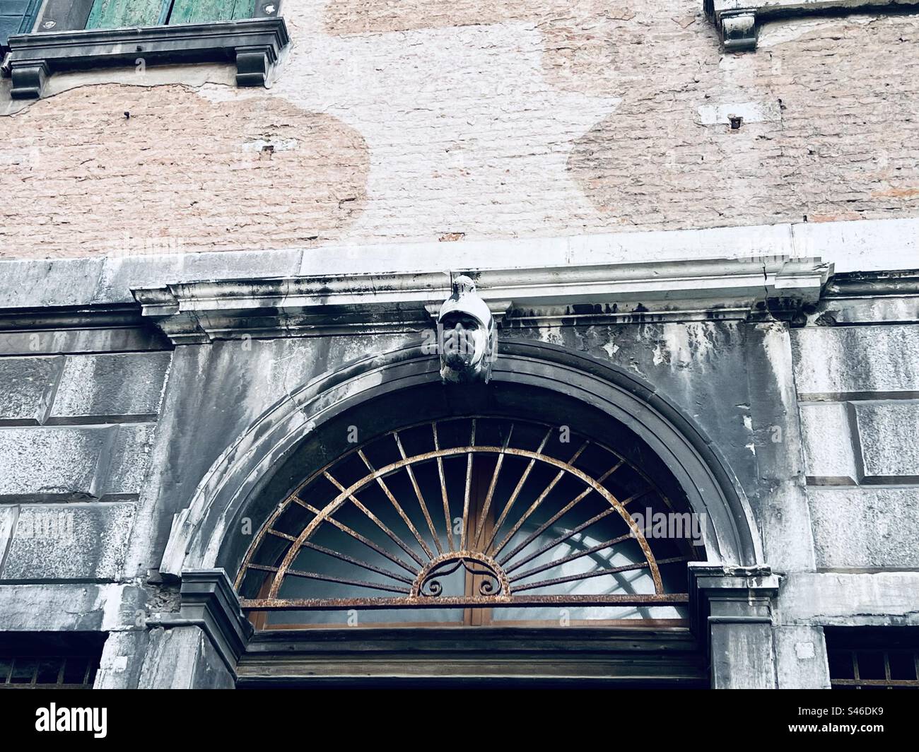 Design in metallo decorato con una piccola testa di pietra su una porta ad arco in un canale di Venezia - Immagine stock catturata con smartphone