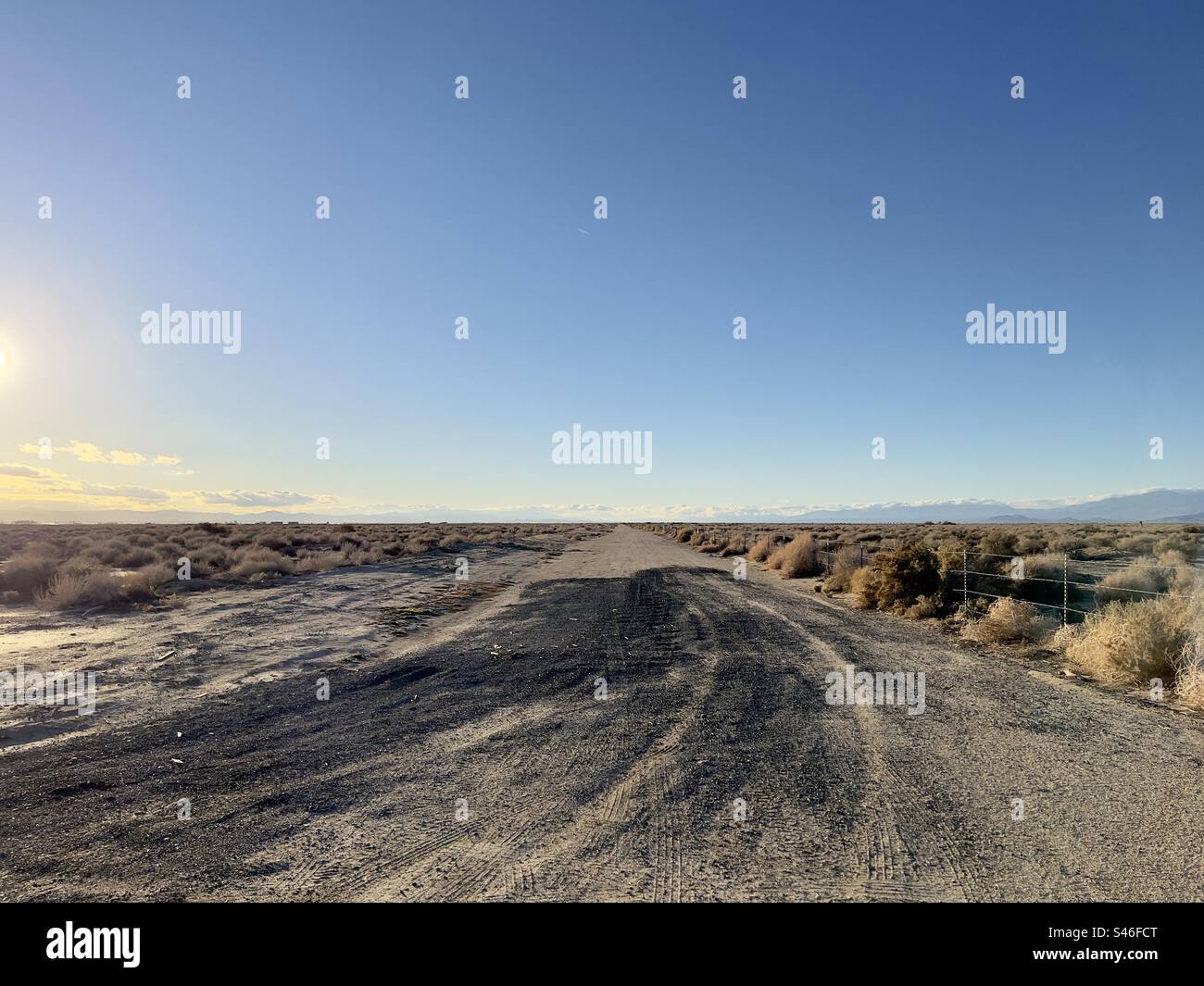 Strada sterrata nel deserto della California meridionale, con il sole ai margini dell'immagine. Cielo blu sopra la testa Foto Stock