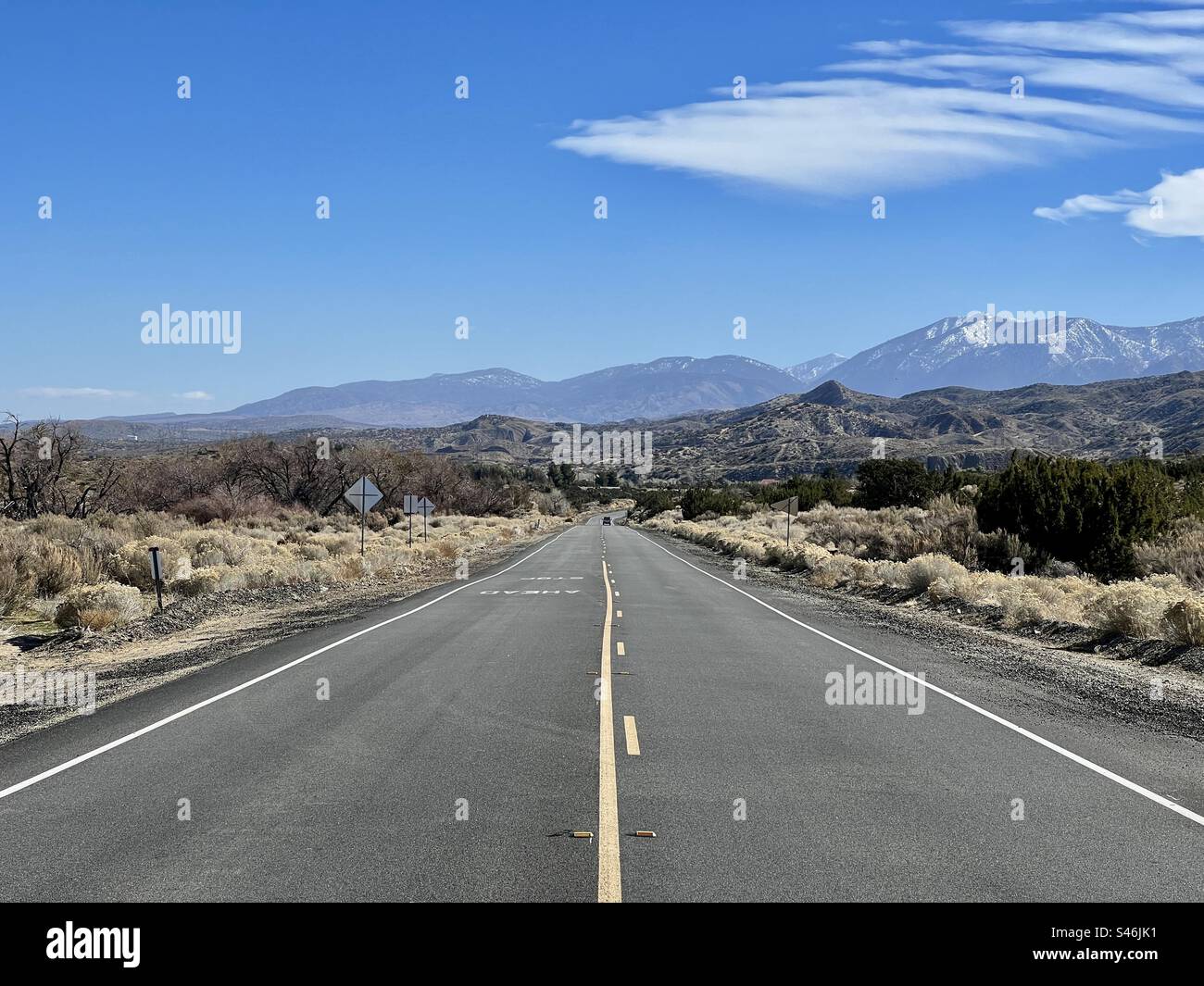 Vista centrale lungo una strada pianeggiante, appena ripavimentata, che conduce alle montagne della California meridionale. Segnaletica orizzontale gialla. Cielo blu sopra la testa Foto Stock
