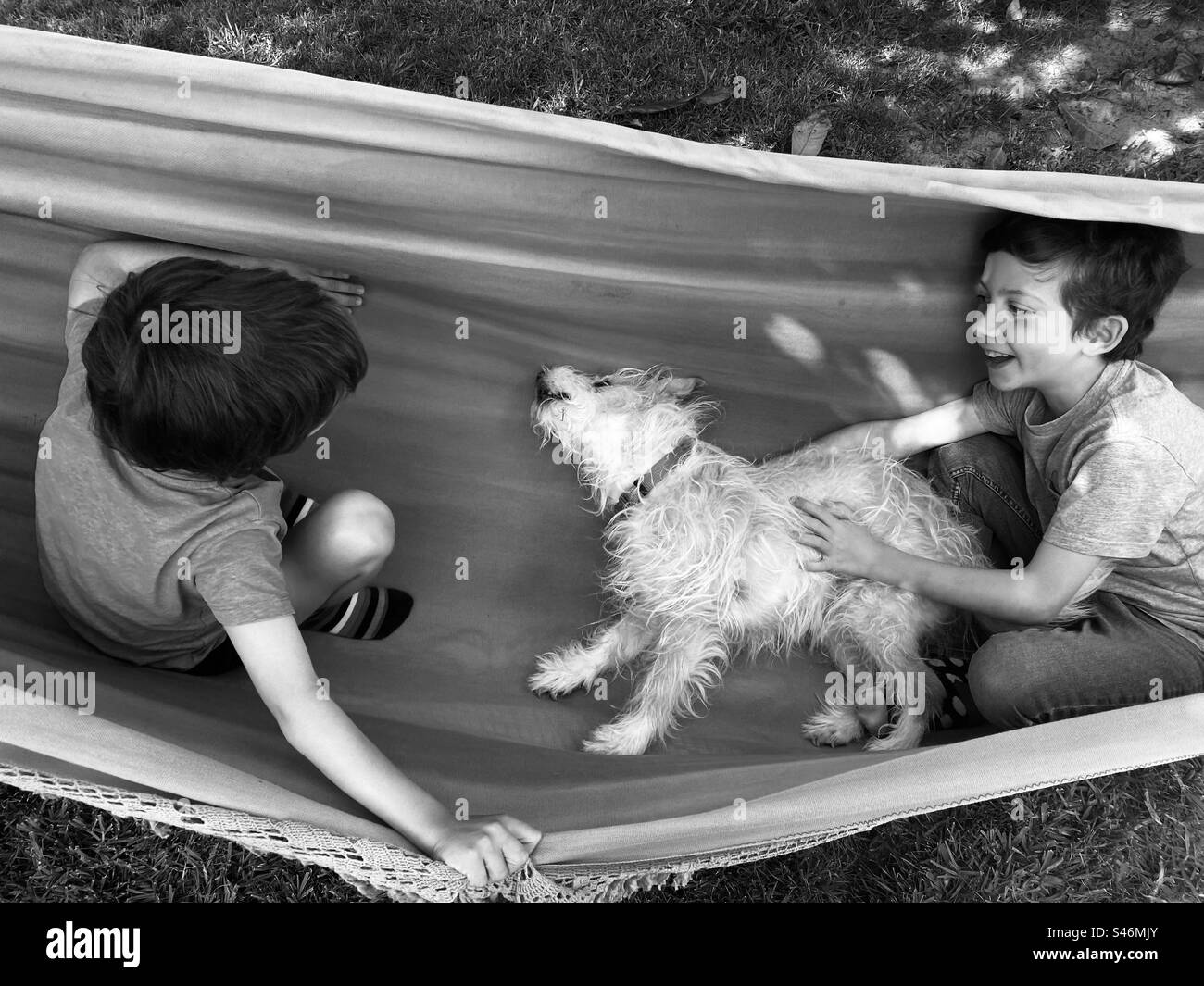 Due fratelli giocano con il loro cane su un'amaca. Lisbona, Portogallo, 2023. Foto Stock