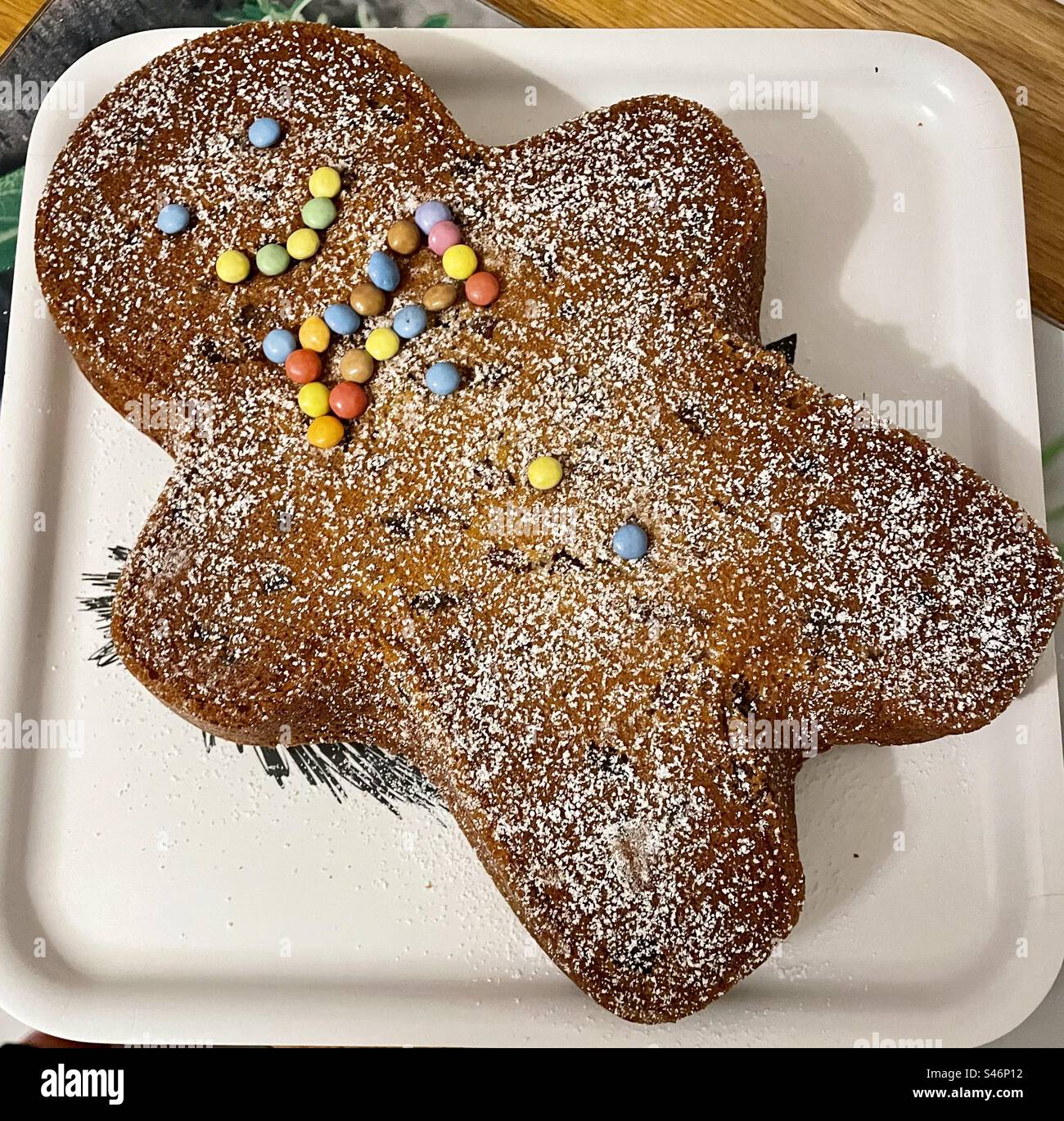Una torta uomo al pan di zenzero con un volto sorridente, realizzata con bonbon M&M, poggia su un vassoio, incarnando gioia, felicità e ricordi preziosi, mentre attende il suo delizioso destino. - Immagine stock catturata con smartphone