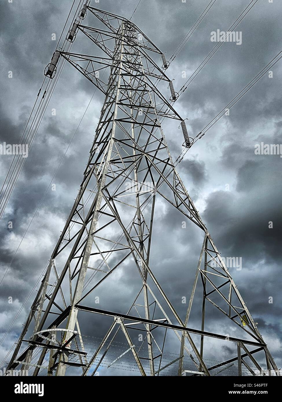 Un traliccio elettrico o una torre di trasmissione che si erge alto sullo sfondo di un cielo oscuro e nuvoloso che cerca di produrre energia elettrica propria sotto forma di fulmini. Foto Stock