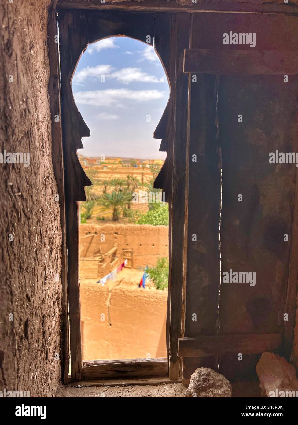 Una vista di un villaggio berbero, deserto e palme viste da una piccola finestra all'interno di una casa di argilla, ad Ait Benhaddou, Marocco Foto Stock