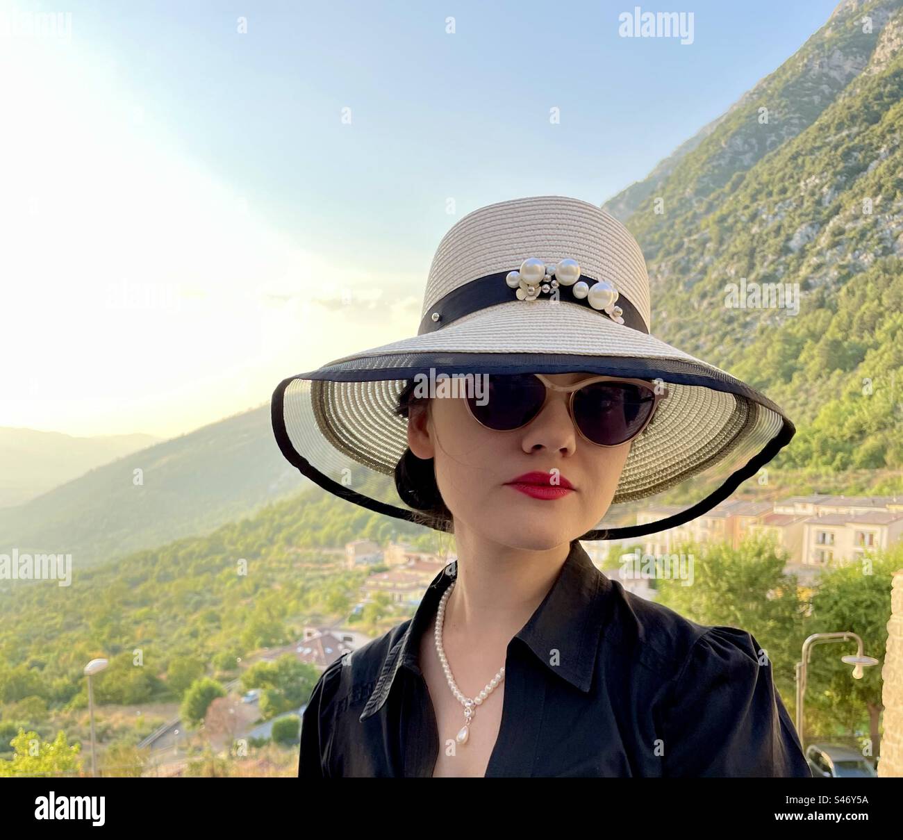 Donna elegante con cappello e occhiali da sole, paesaggio al tramonto Foto Stock