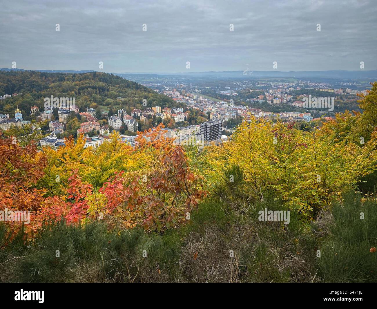 Vista panoramica di Karlovy Vary circondata da colline con alberi dai colori autunnali in primo piano. - Immagine stock catturata con smartphone