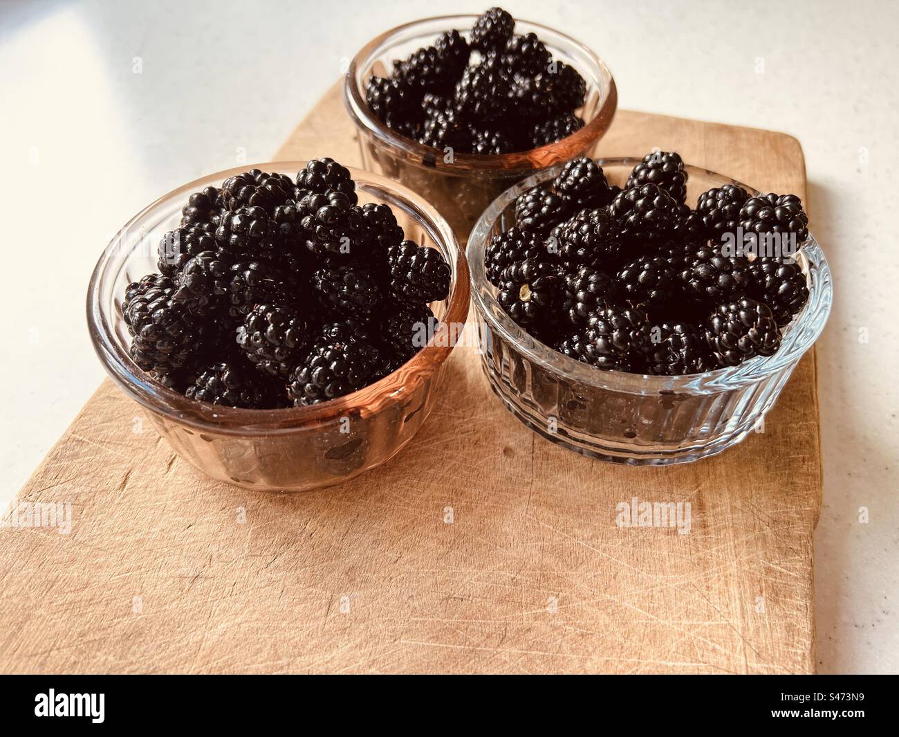 Primo piano obliquo di more ricoperte da tre piatti di vetro circolari su una tavola di legno. Frutta foraggiata, di provenienza locale, nutriente. - Immagine stock catturata con smartphone