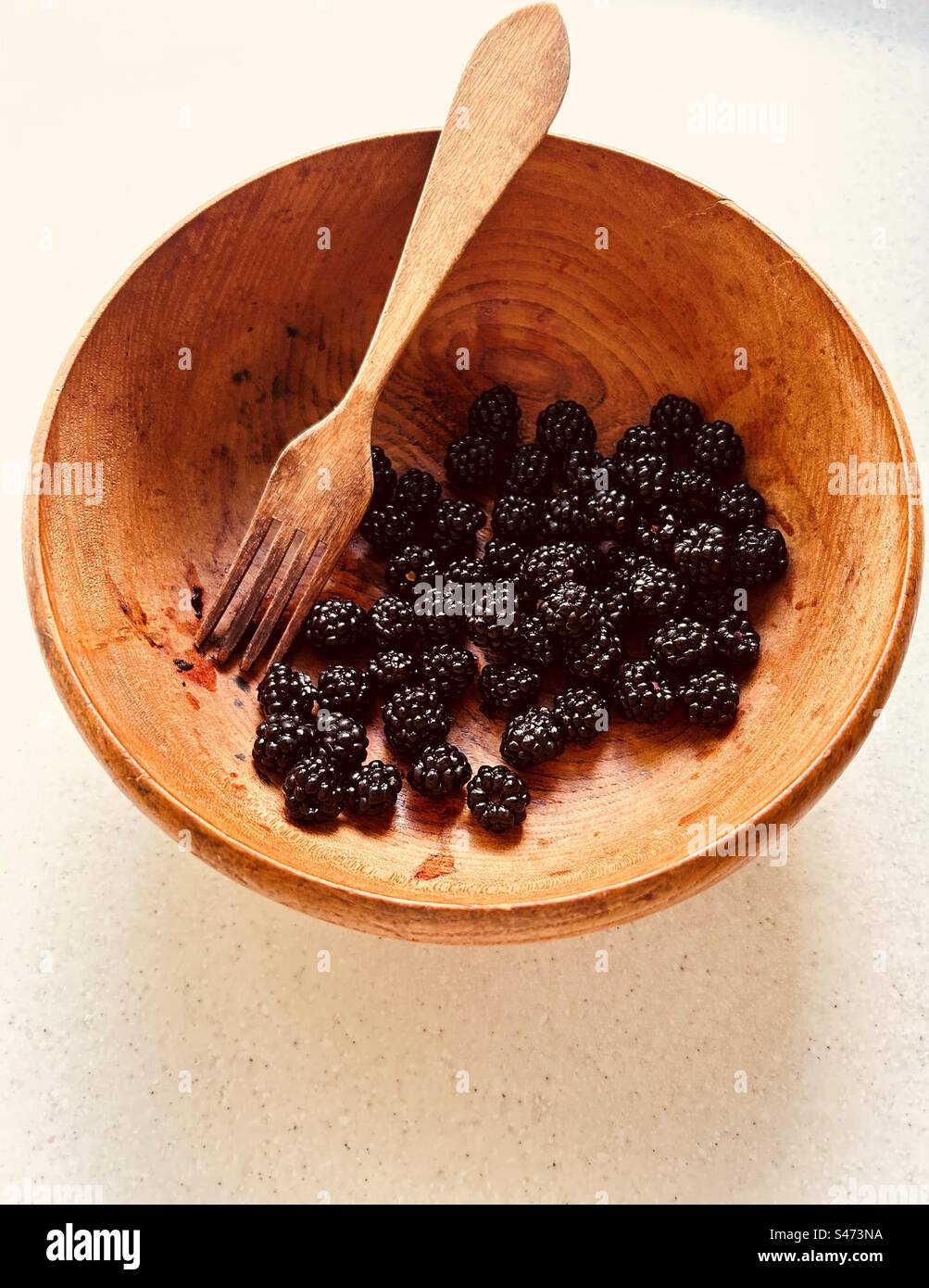 More e forchetta di legno in una ciotola di legno granato. Frutta foraggiata, di provenienza locale, nutriente. - Immagine stock catturata con smartphone