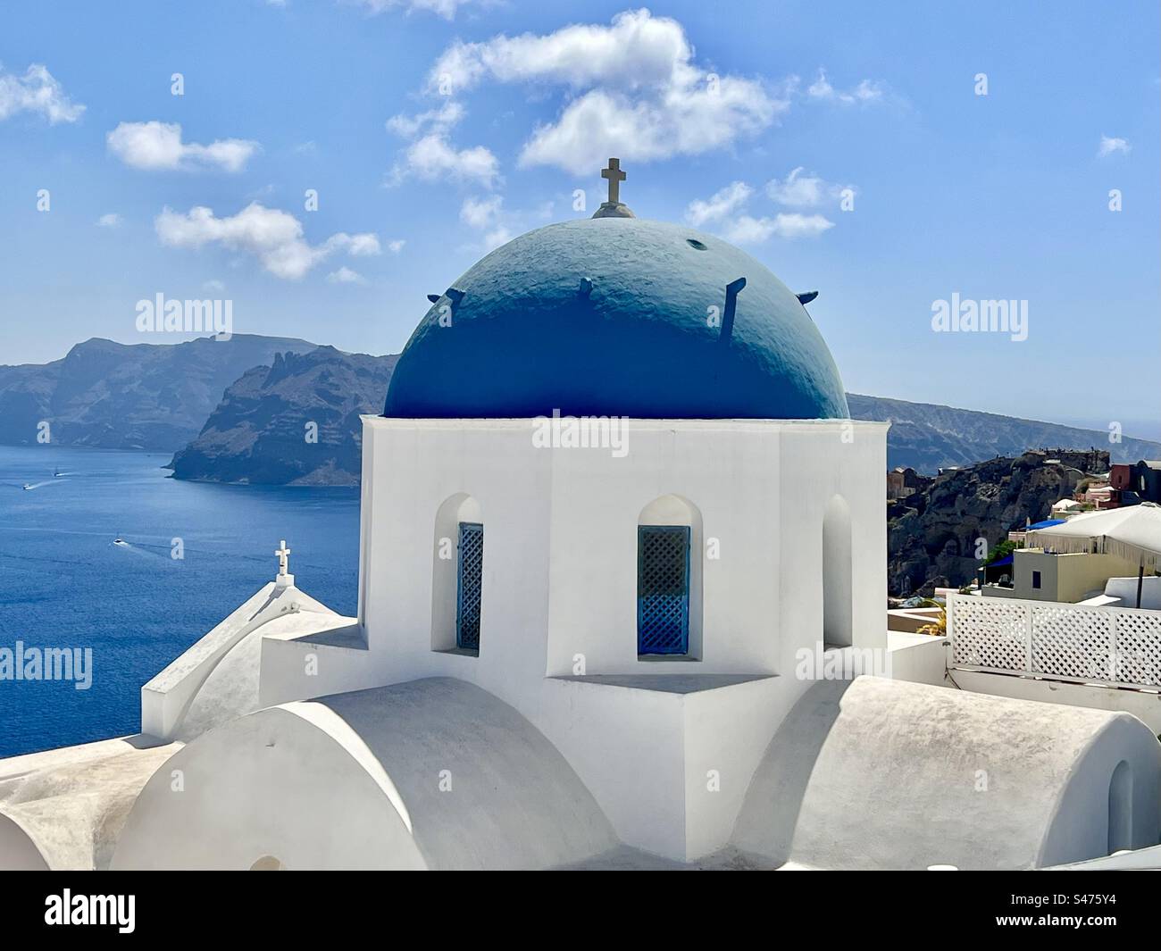 La chiesa a cupola blu imbiancata, Sant'Anastasi, contro il cielo blu e l'acqua blu della caldera sottostante a Santorini. Foto Stock