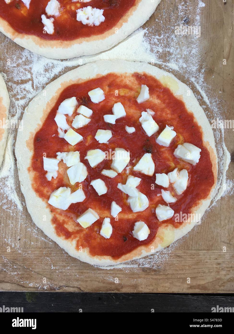 Pizza Margherita pronta per essere informata. Pizza italiana, mozzarella di pizza, pomodoro e origano. Su spianatoia di legno infarinata. Foto Stock