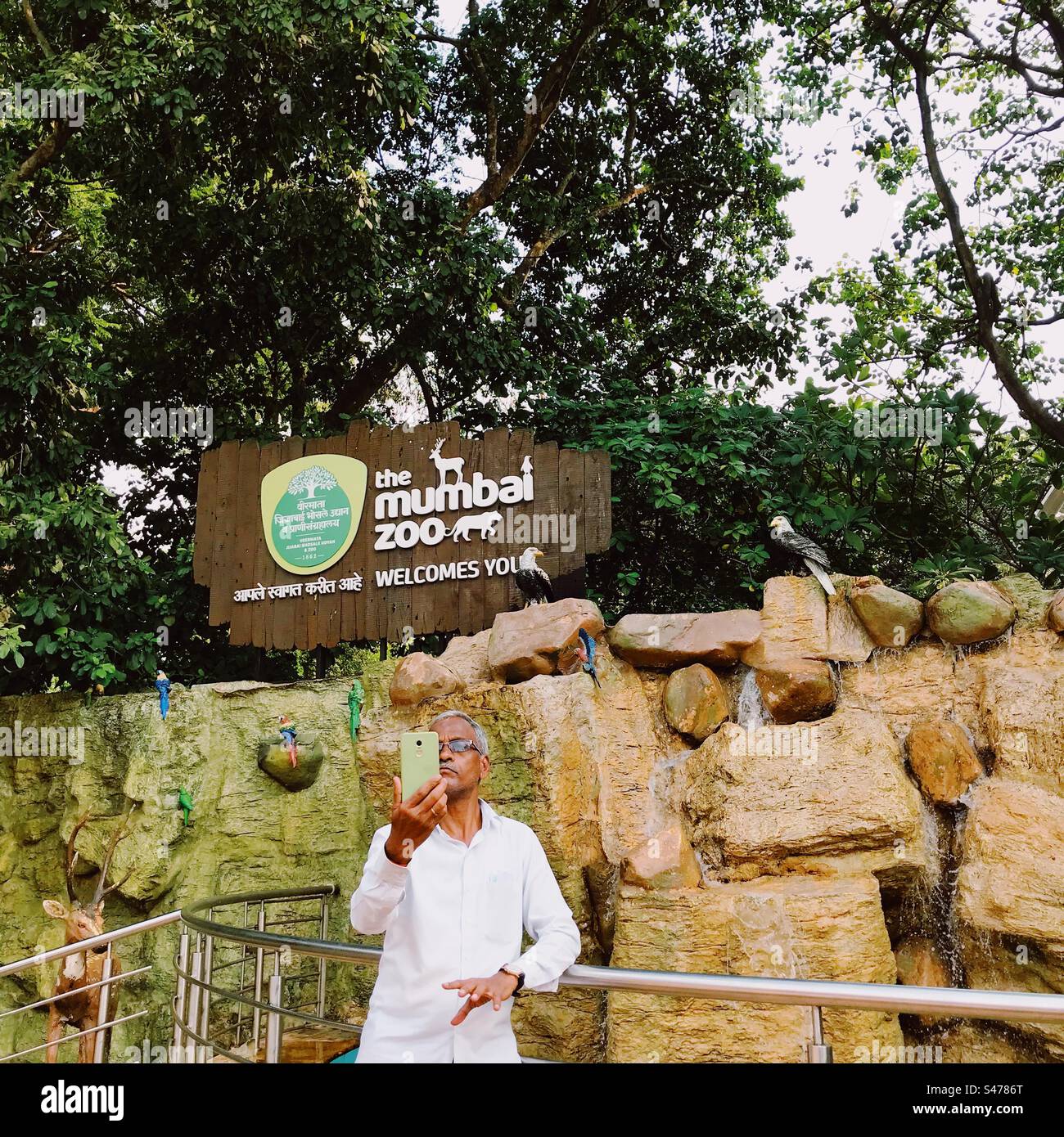 Un anziano indiano che fa un selfie di se stesso davanti all'insegna dello zoo di Mumbai in India Foto Stock