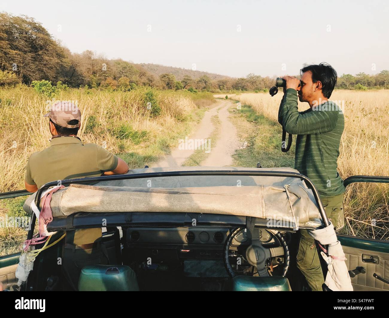 Due uomini avvistano la fauna selvatica attraverso il binocolo in una giungla in India - Immagine stock catturata con smartphone