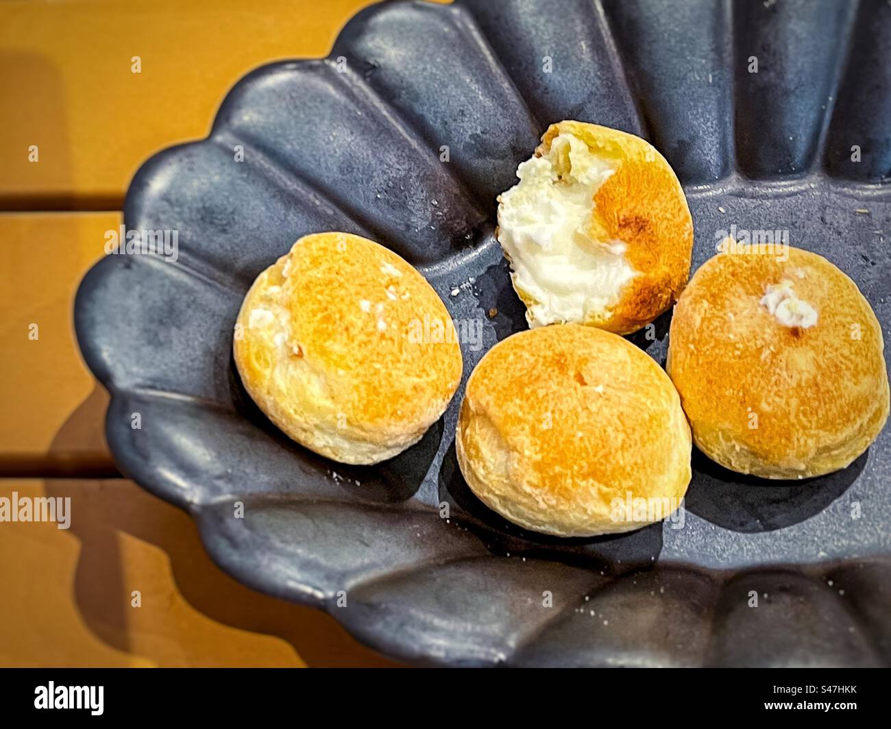 Vista ad alto angolo di mini pompini di crema alla vaniglia in ciotola nera su un tavolo di legno giallo. Foto Stock