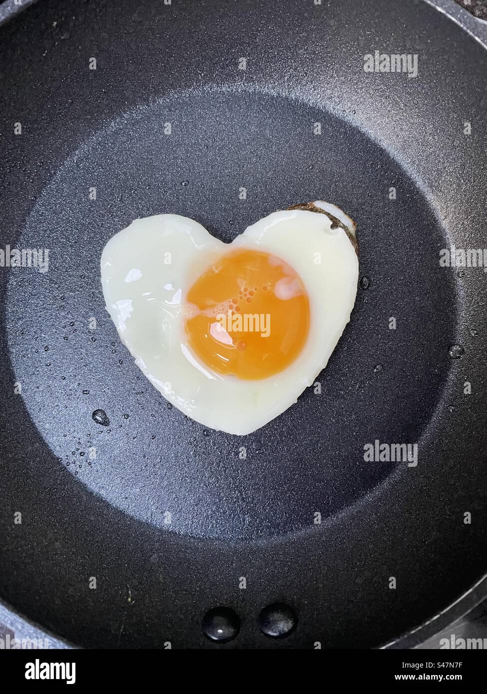 Uovo fritto a forma di cuore in una padella piccola Foto Stock