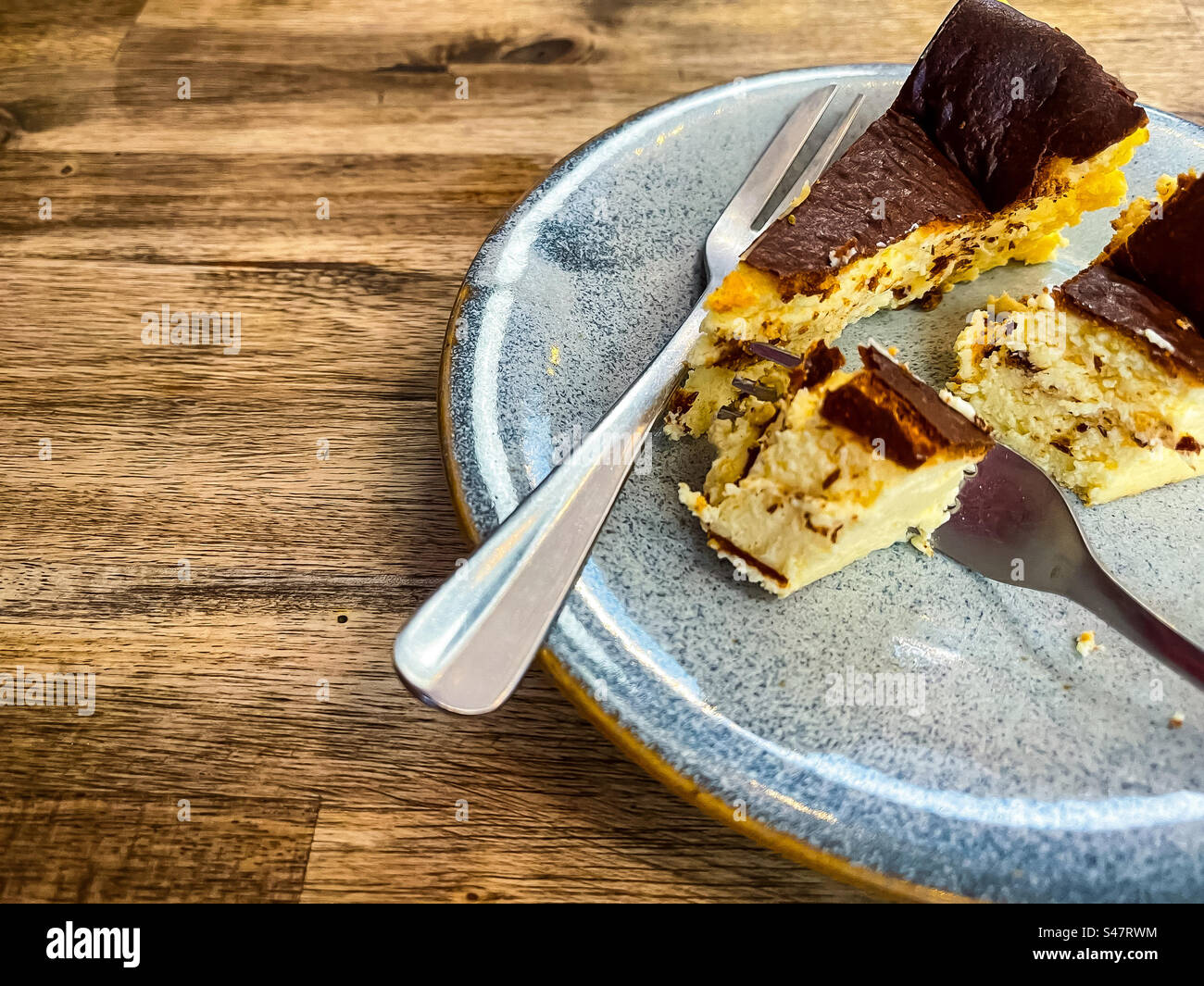 Primo piano di una fetta di cheesecake basca tagliata con due forchette sul piatto su un tavolo di legno. Toni marroni. Foto Stock