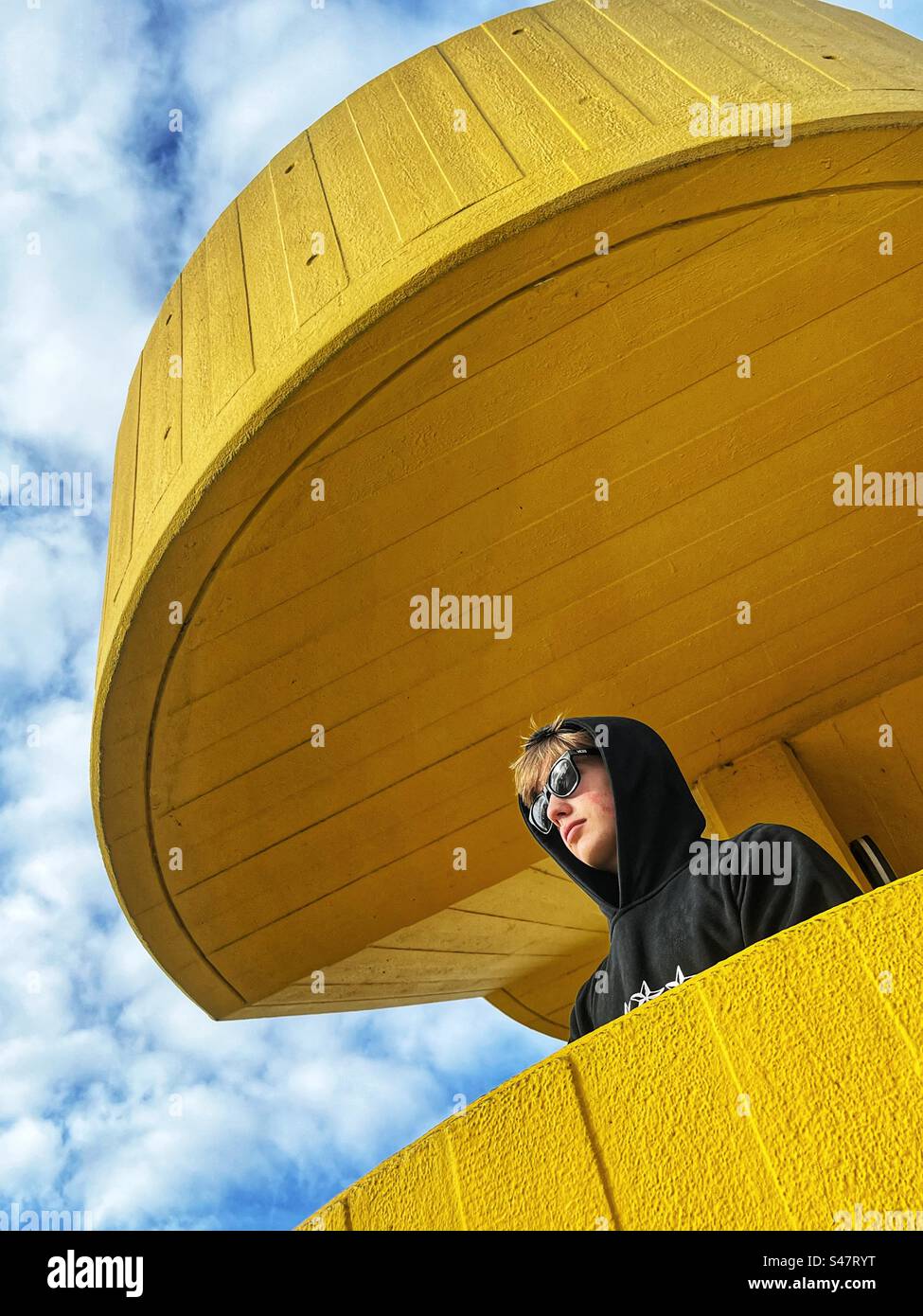 Un ragazzo che indossa una felpa con cappuccio e occhiali da sole posa per una foto su una scala gialla sulla Southbank a Londra, in Inghilterra. Foto Stock